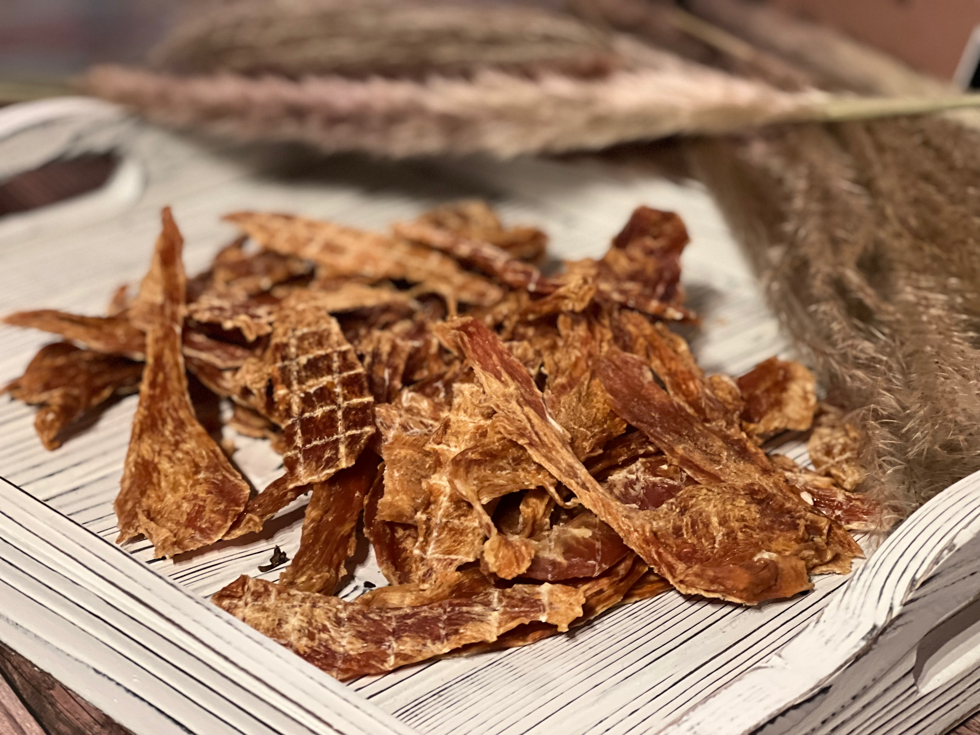 Pile of PupChew dehydrated chicken breast jerky strips on a white wooden tray
