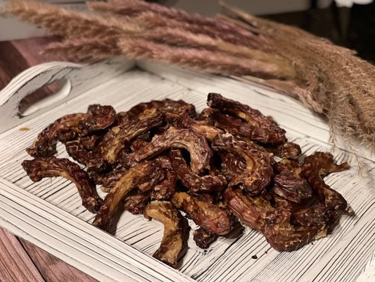 Pile of PupChew dehydrated chicken neck dog treats on a white wooden tray