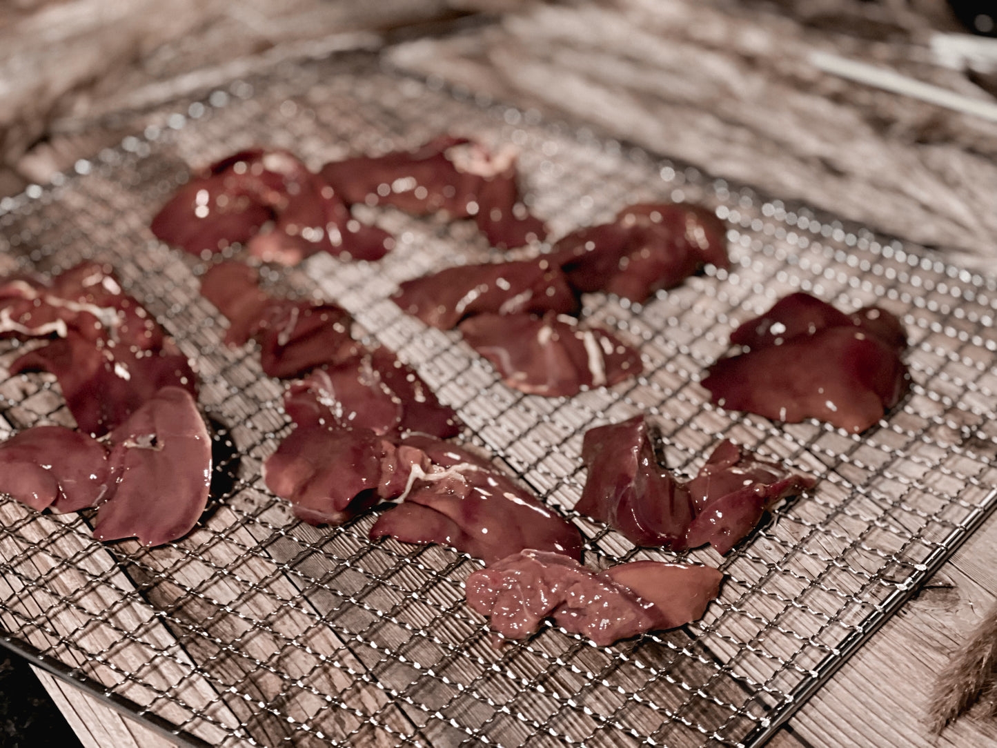 Raw chicken liver pieces arranged on a mesh dehydrator rack
