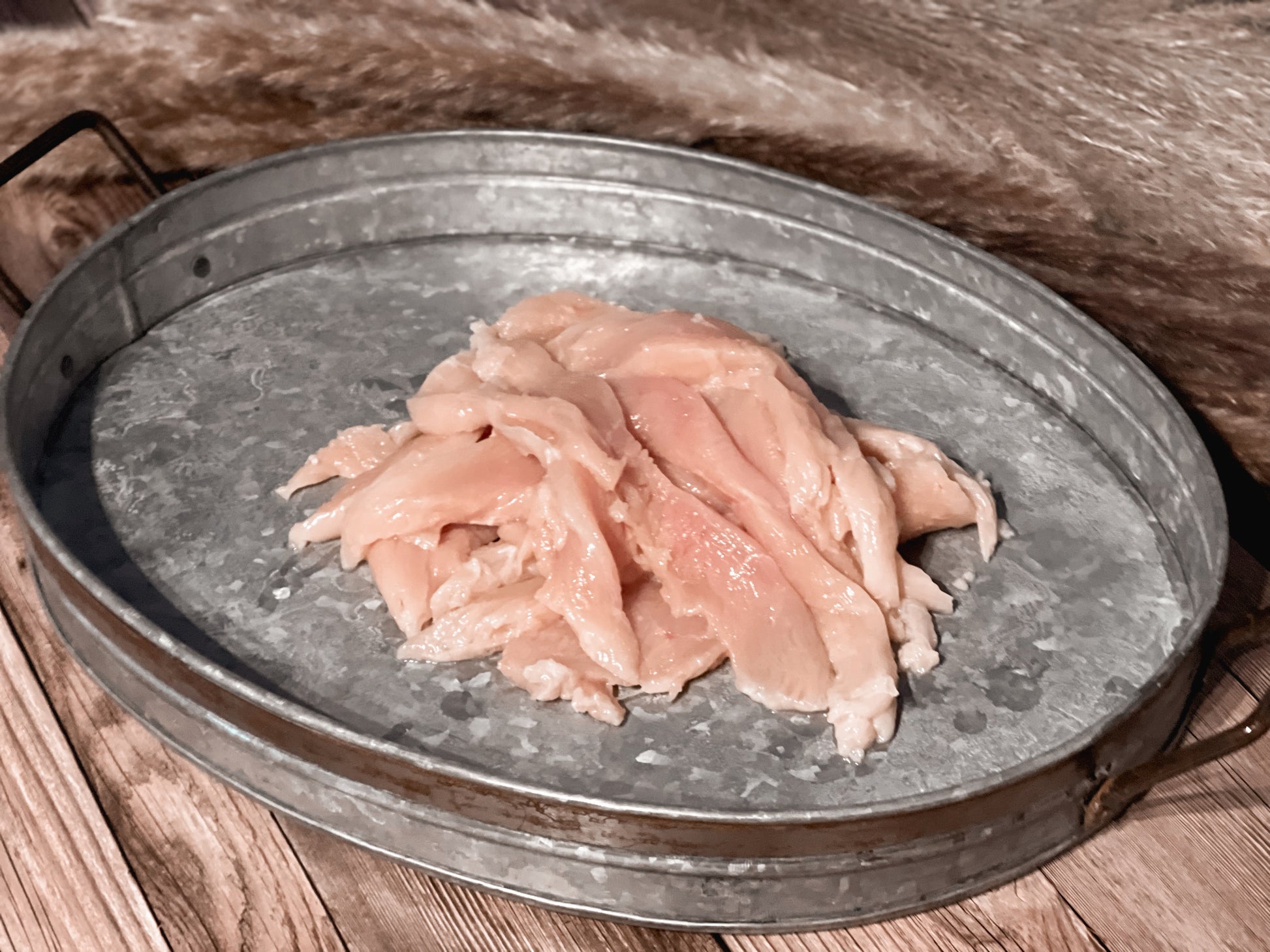 Thinly sliced raw chicken breast in a galvanized metal tray before dehydration